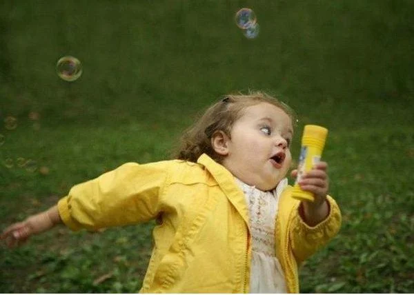 Toddler girl in a yellow raincoat running with a bubble wand
