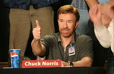 Chuck Norris giving a thumbs up at a table with his nameplate