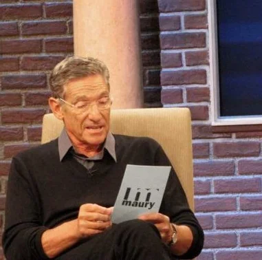 Maury Povich reading results from a card on his talk show set